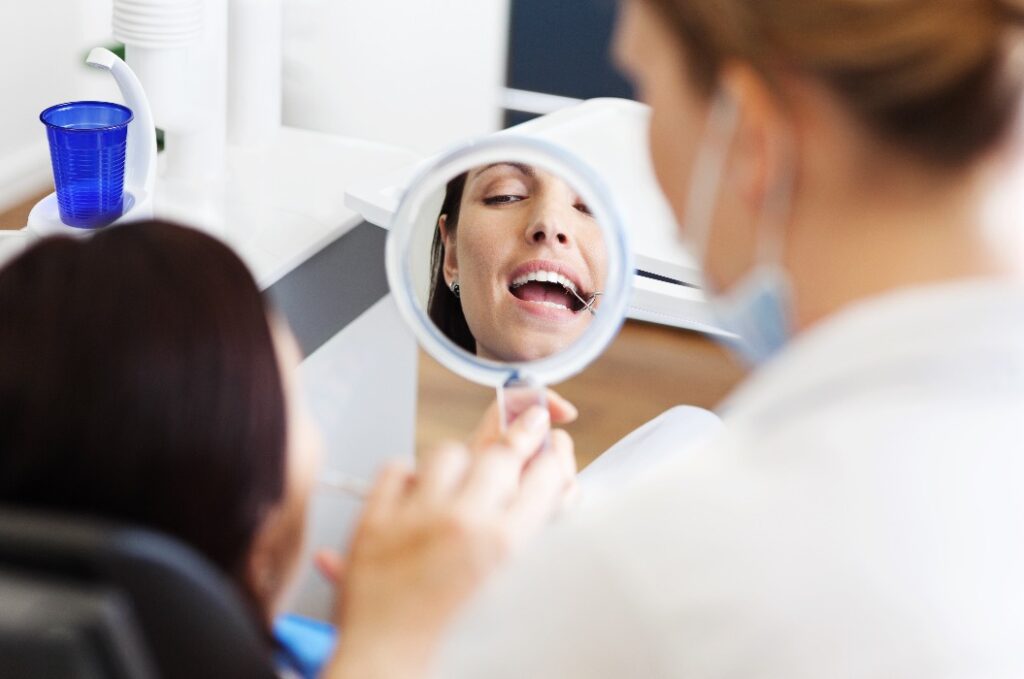 frau beim zahnarzt schaut nach der Zahnprophylaxe in einen spiegel