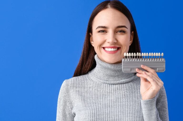 Junge Frau mit Zahnfarbskala vor blauem Hintergrund